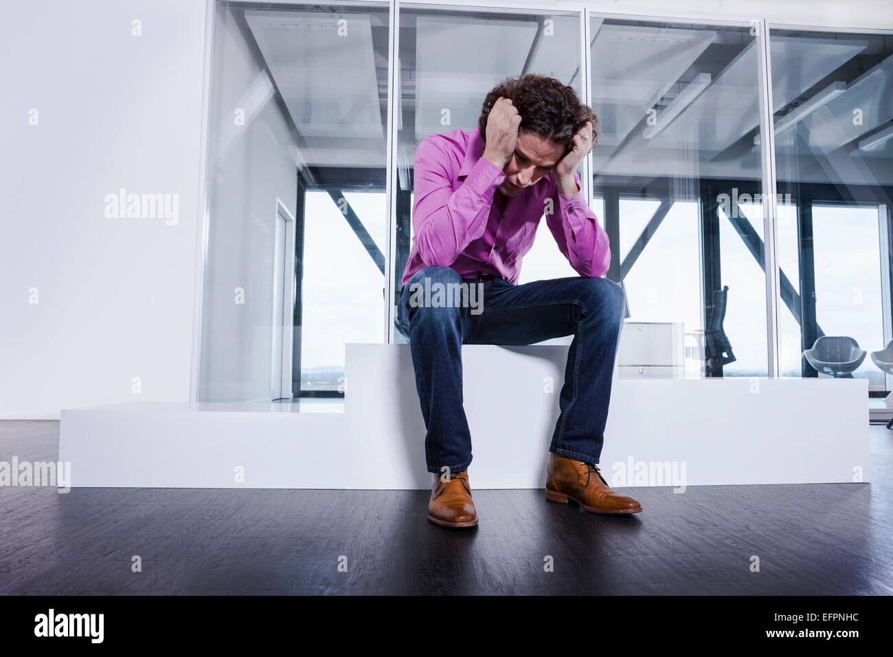 Uomo maturo seduto sul podio con testa in mani Foto Stock