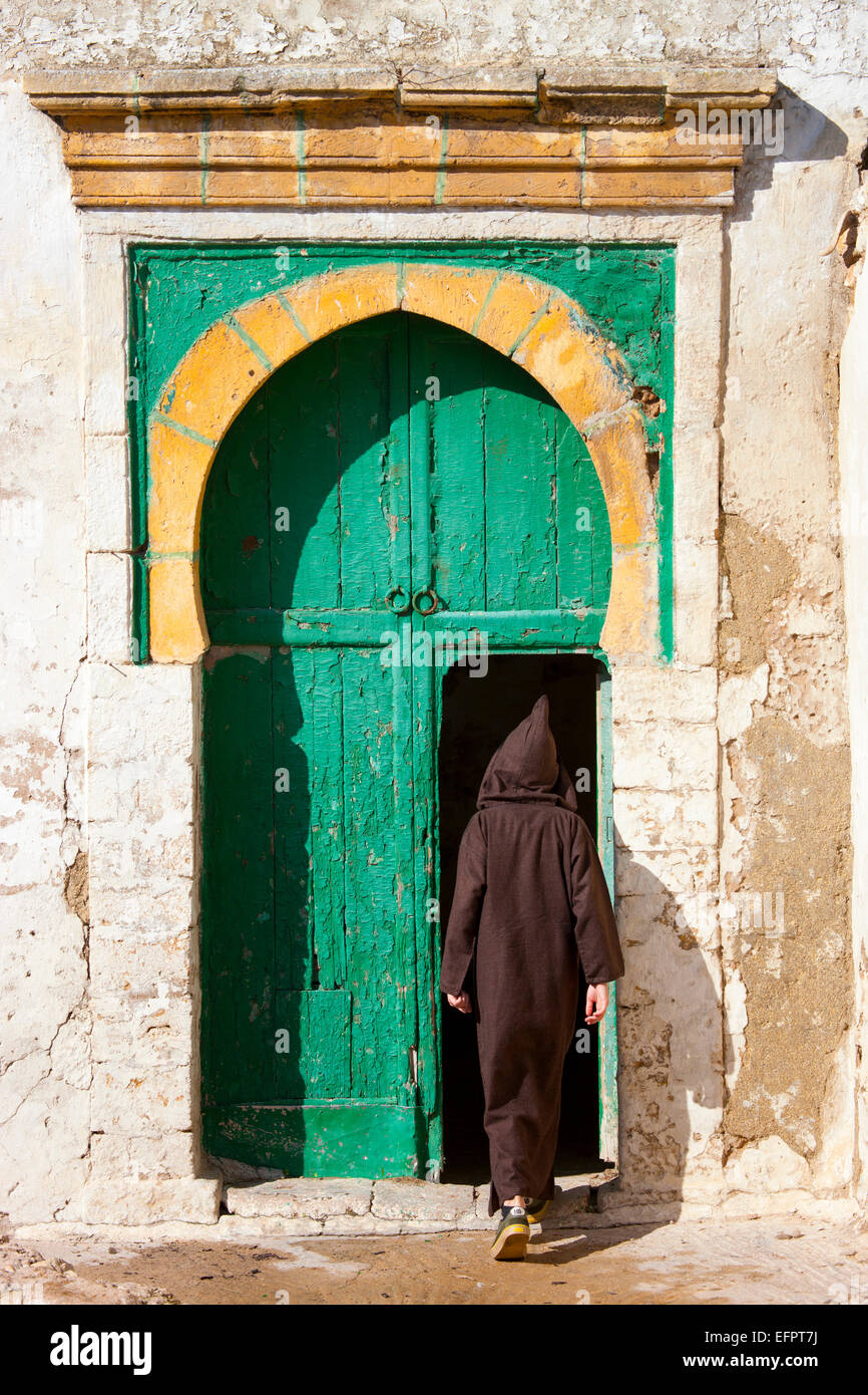 Vista posteriore di uomo che indossa abiti tradizionali il rafforzamento in porta, Essaouira, Marocco Foto Stock