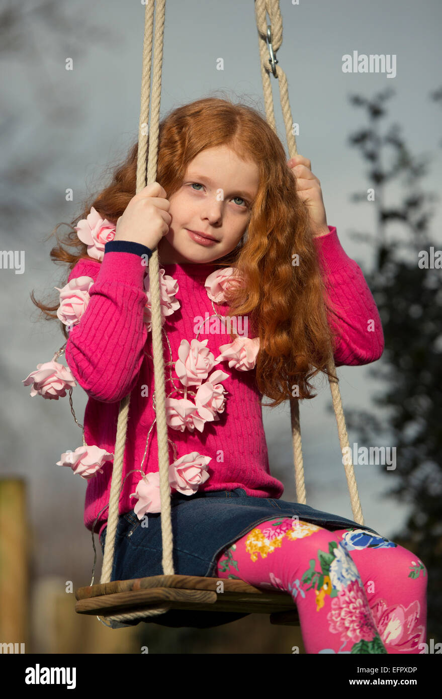 Ritratto di una bambina con una ghirlanda di rose intorno al suo collo su uno swing Foto Stock