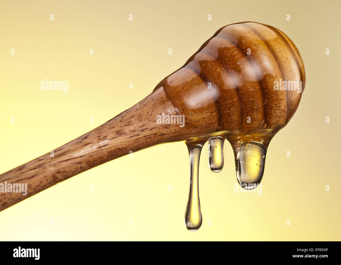Gocce di miele che fluisce dal bastone di legno su sfondo giallo. Foto Stock