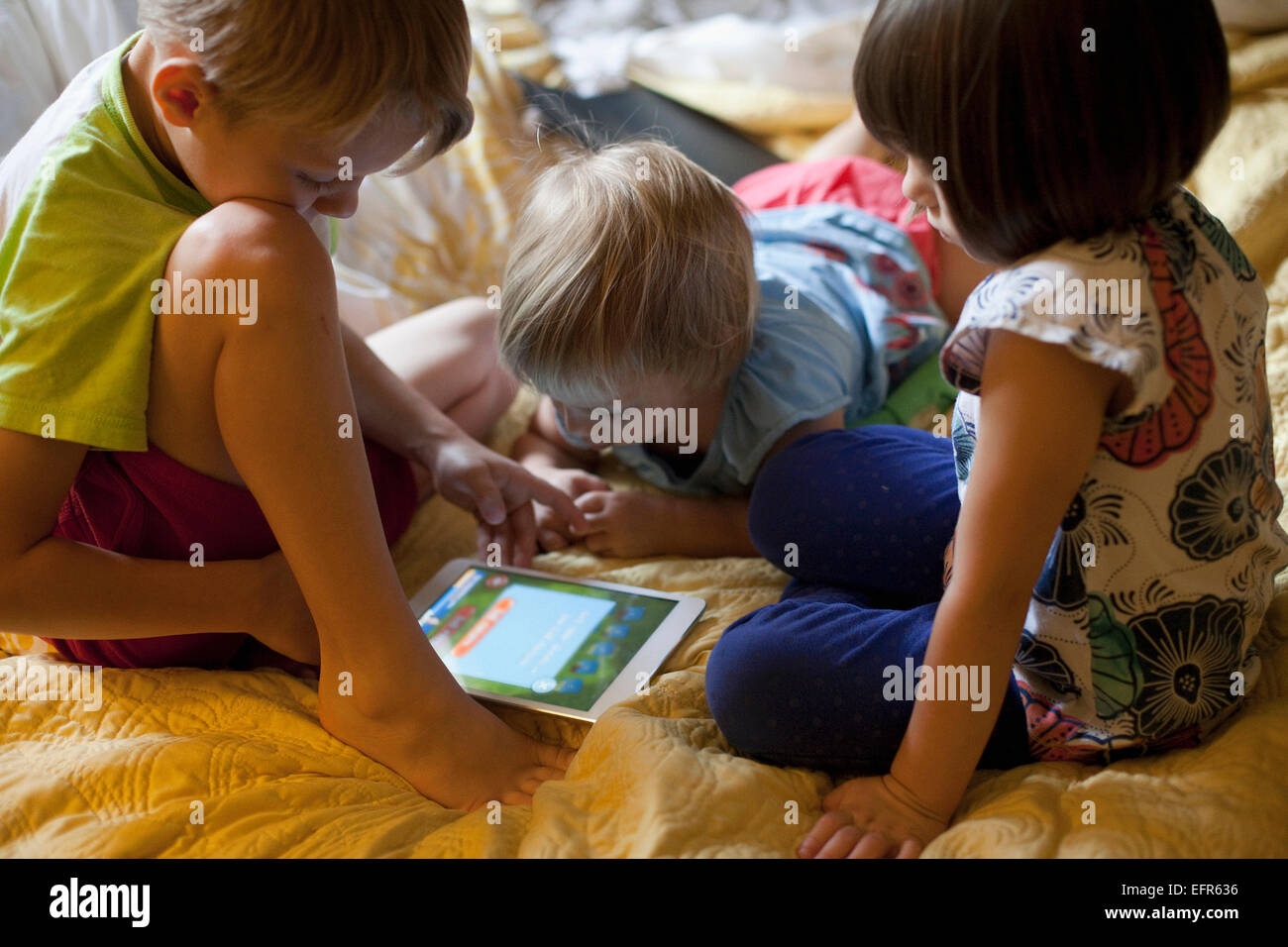 Tre bambini relax su letto tramite tavoletta digitale Foto Stock