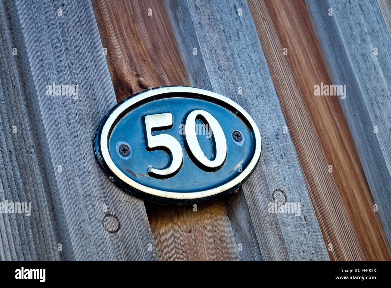Il numero 50 su un ottone & smalto targhetta fissata al legno parete a stecche di una casa a significare indirizzo Foto Stock