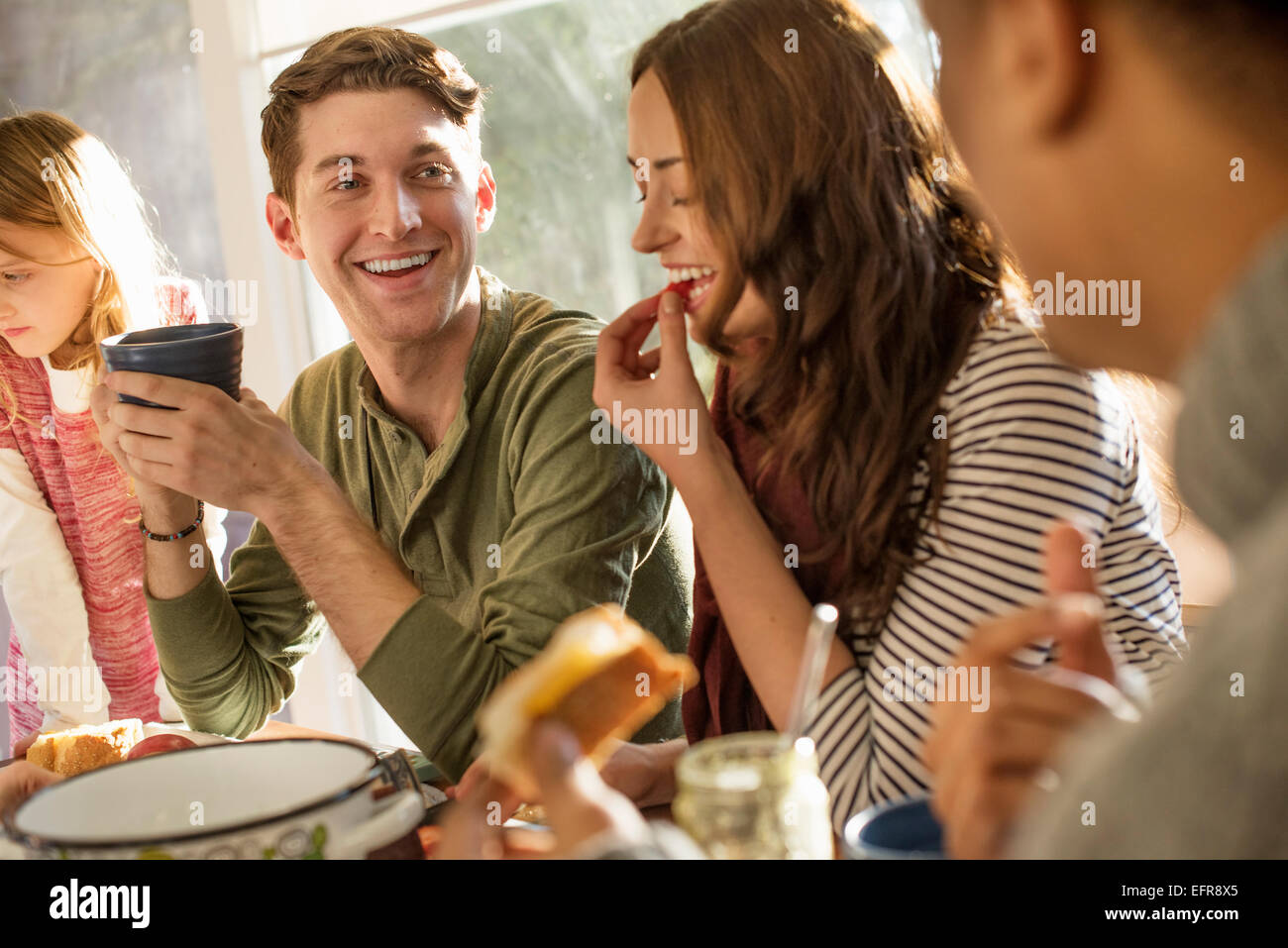 Un gruppo di persone sedute a un tavolo, sorridente, mangiando, bevendo e chiacchierando. Foto Stock