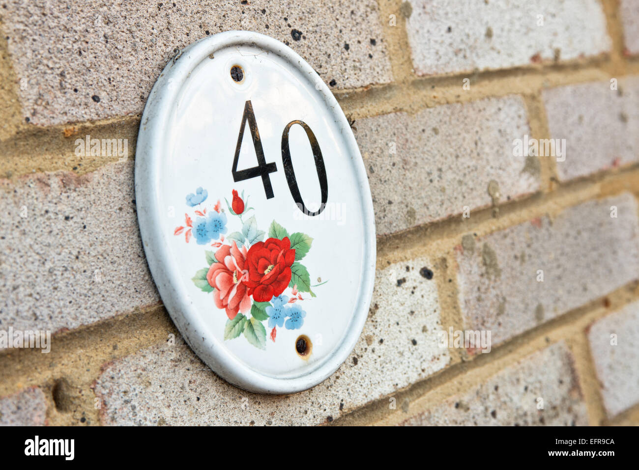 Il numero 40 su un piatto di portata in ceramica bianca con disegno floreale, attaccato al muro di mattoni di una casa a significare indirizzo Foto Stock