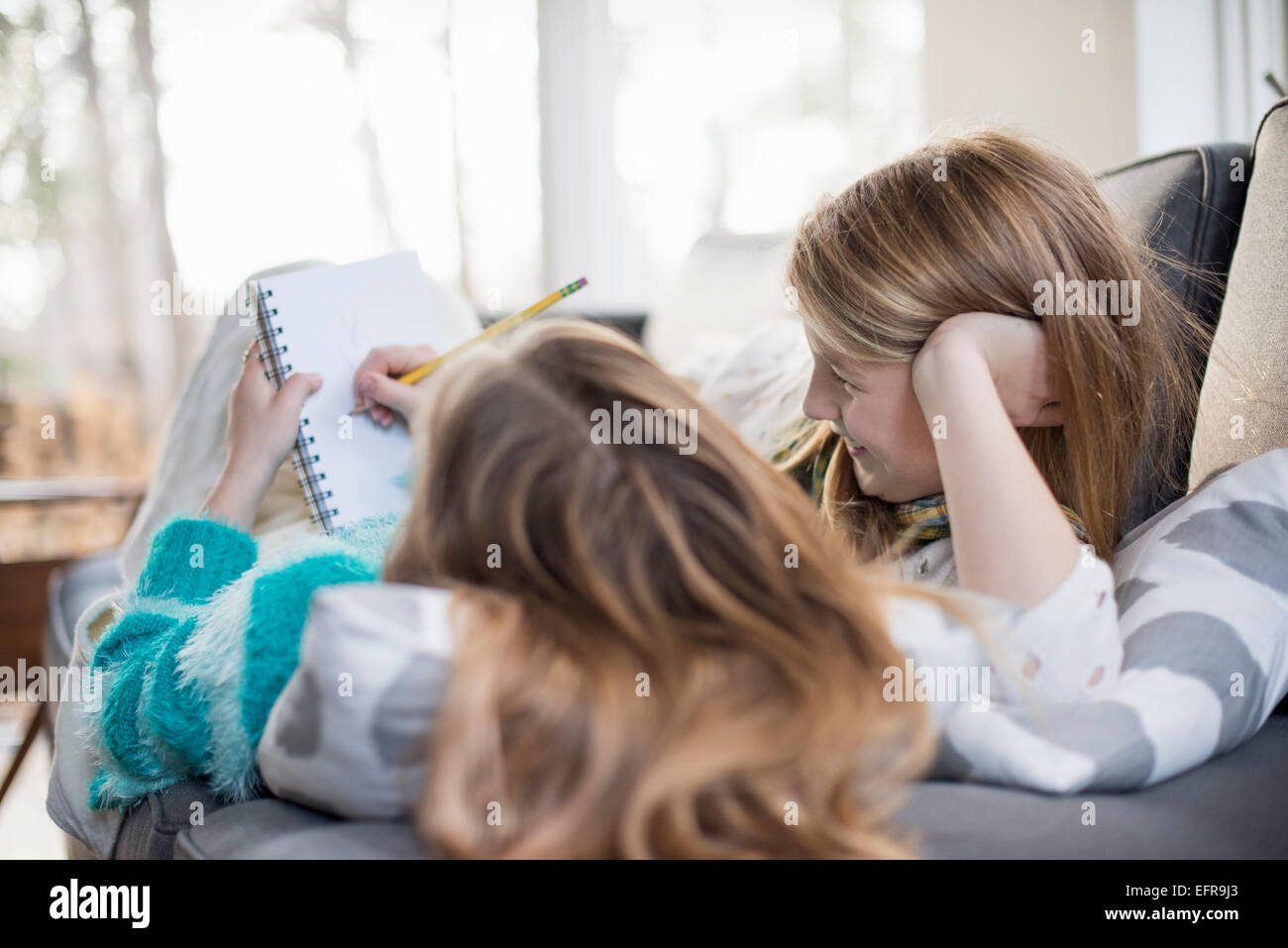 Due ragazze giacente su un divano, una scrittura in un notebook con una matita. Foto Stock