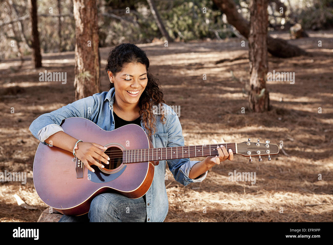 Giovane donna seduta nella foresta suonare la chitarra acustica Foto Stock
