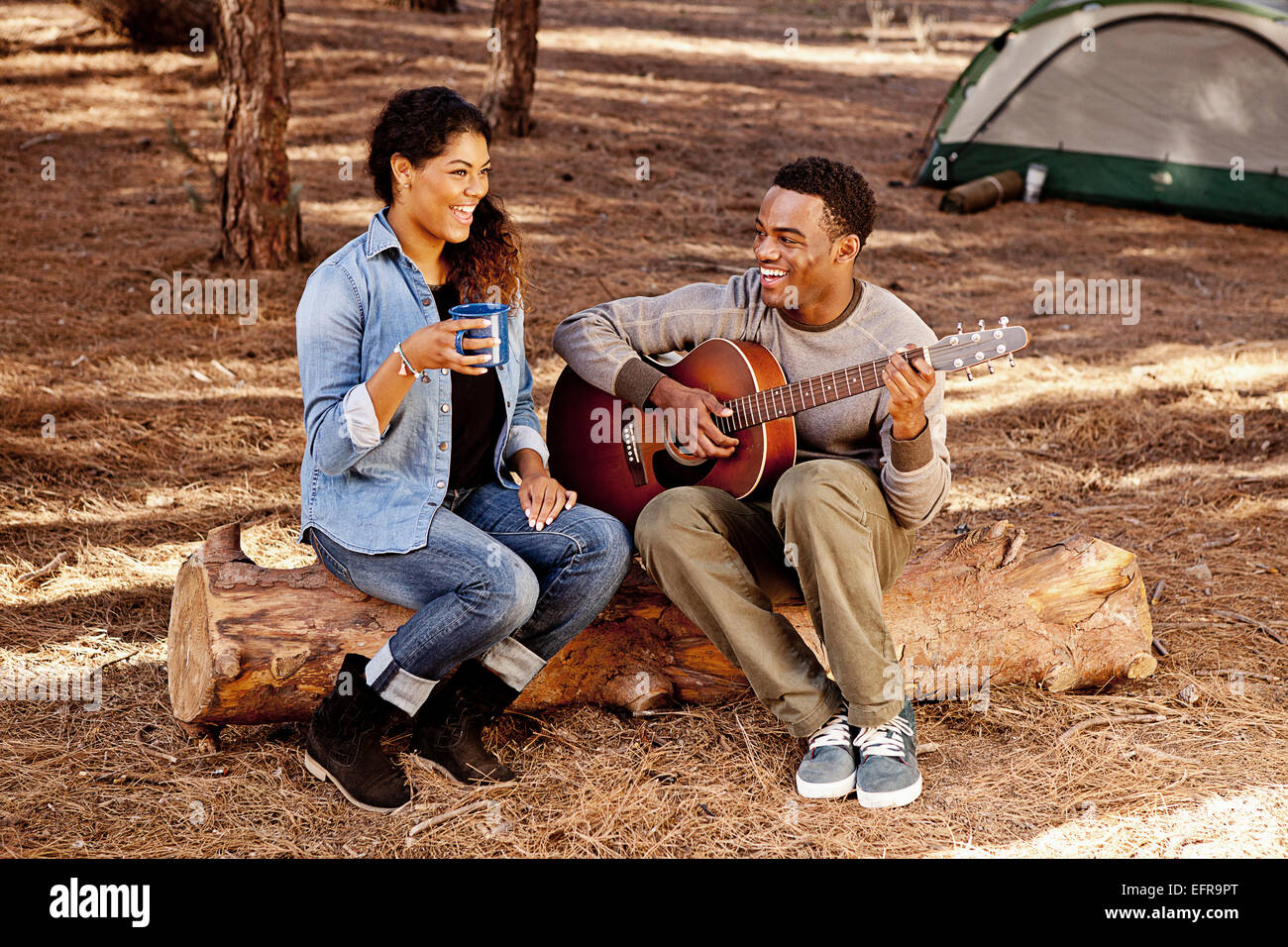 Coppia giovane seduto sul registro di foresta di suonare la chitarra acustica Foto Stock