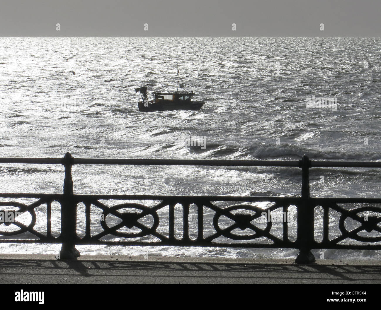 Una barca da pesca di lotte contro un westerly tide off Brighton nelle prime ore del mattino la luce del sole durante il luccicante mare. Foto Stock