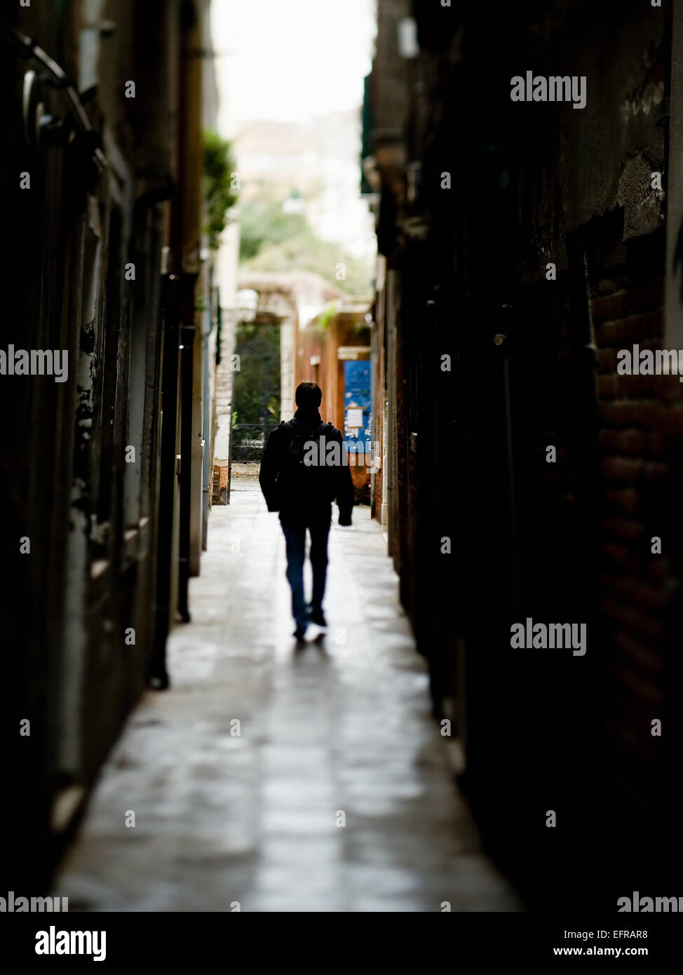 Silhouette di un uomo che cammina verso il basso un vicoletto a Venezia, tra case storiche. La Serenissima, nel centro storico della città Foto Stock