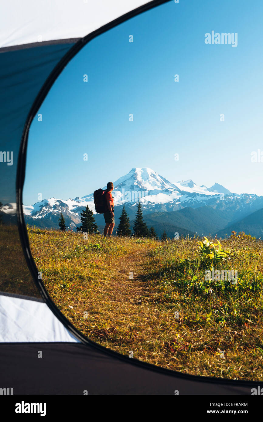 Vista dall'interno di una tenda da campeggio di un uomo che passeggia attraverso la foresta nazionale di terra con il Monte Baker nella distanza. Foto Stock