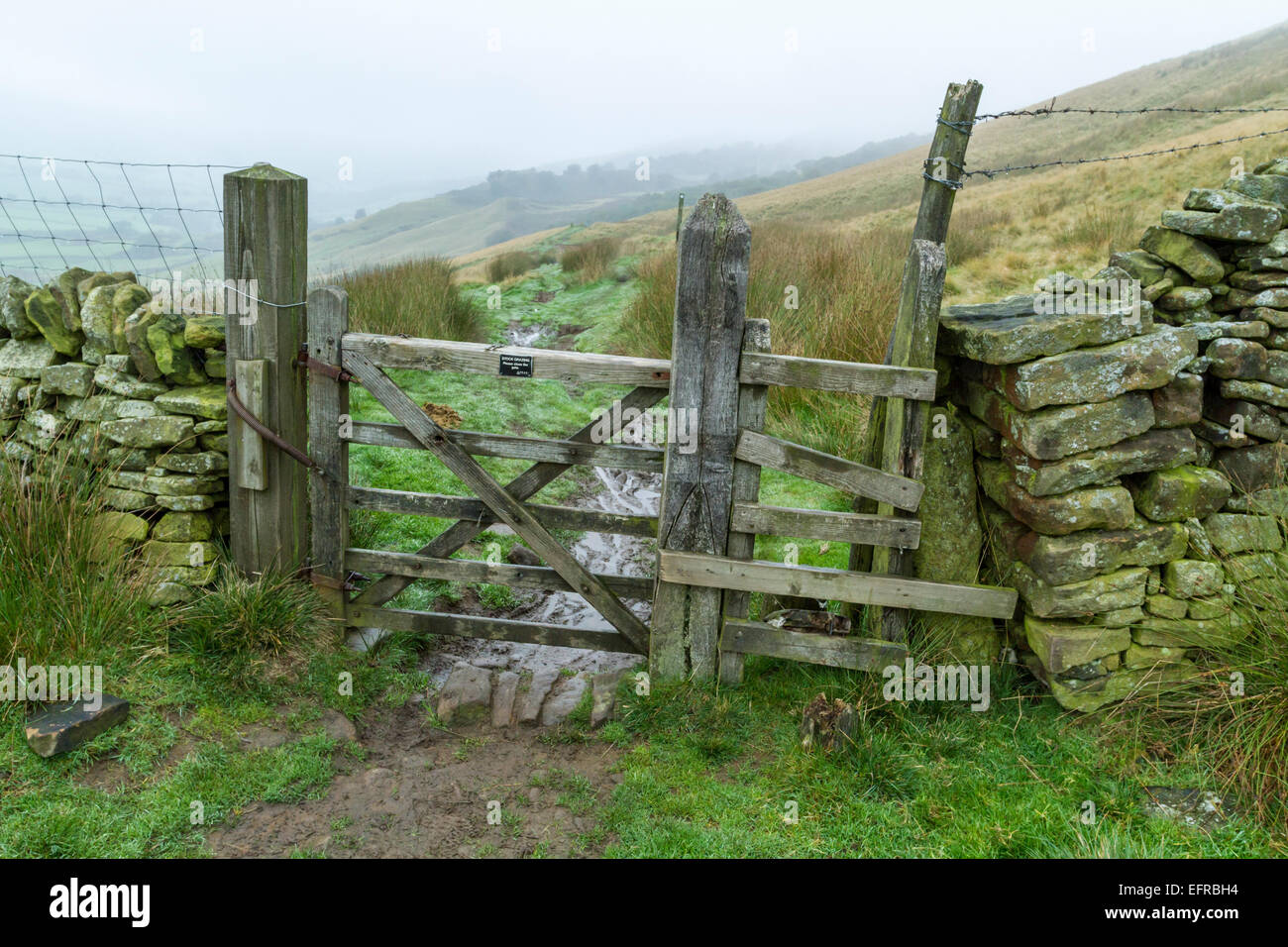 Giornata uggiosa in campagna. Cancello in legno su un umido sentiero fangoso con la nebbia sulle colline del Derbyshire, England, Regno Unito Foto Stock