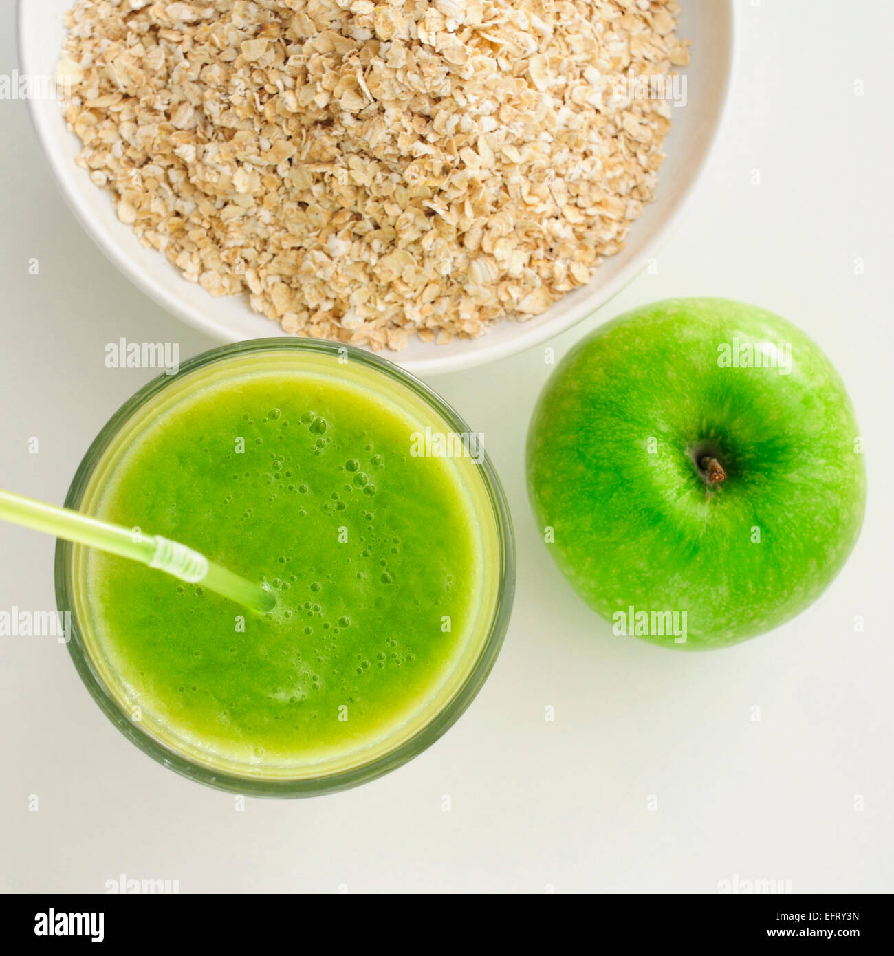 Alta angolazione di un Apple, un vetro con un frullato di verde e di una ciotola con farina di avena dei cereali su un tavolo bianco Foto Stock