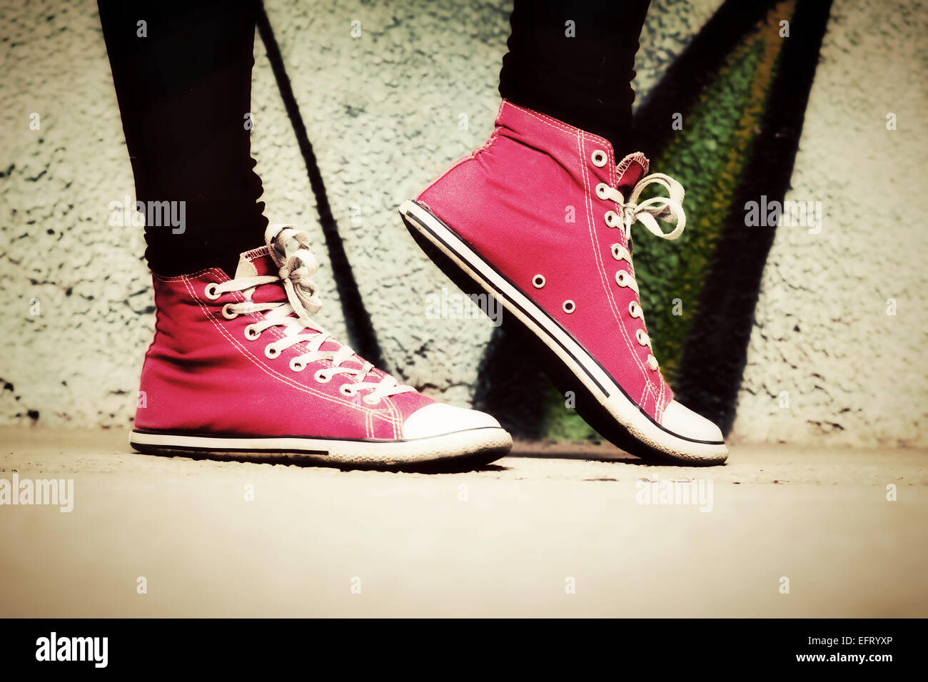 Close up di rosa sneakers indossata da un adolescente. Grunge muro di graffiti, rétro in stile vintage Foto Stock