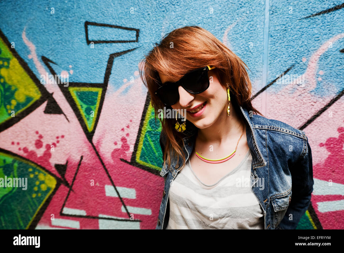 Elegante ragazza alla moda nella camicia di jeans ritratto colorato contro il muro di graffiti. Moda, tendenze, sottocultura. Foto Stock