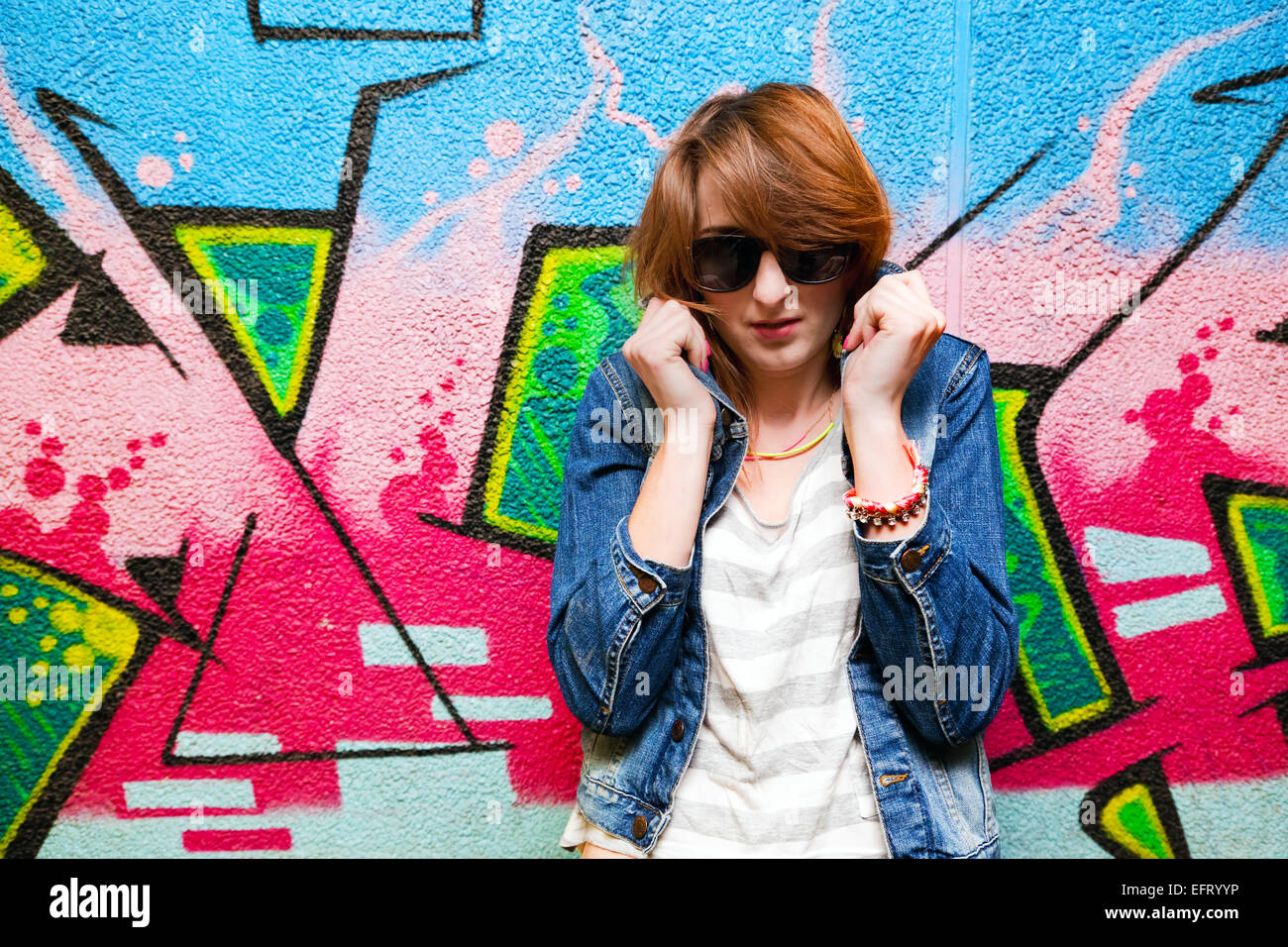 Elegante ragazza alla moda nella camicia di jeans ritratto colorato contro il muro di graffiti. Moda, tendenze, sottocultura. Foto Stock