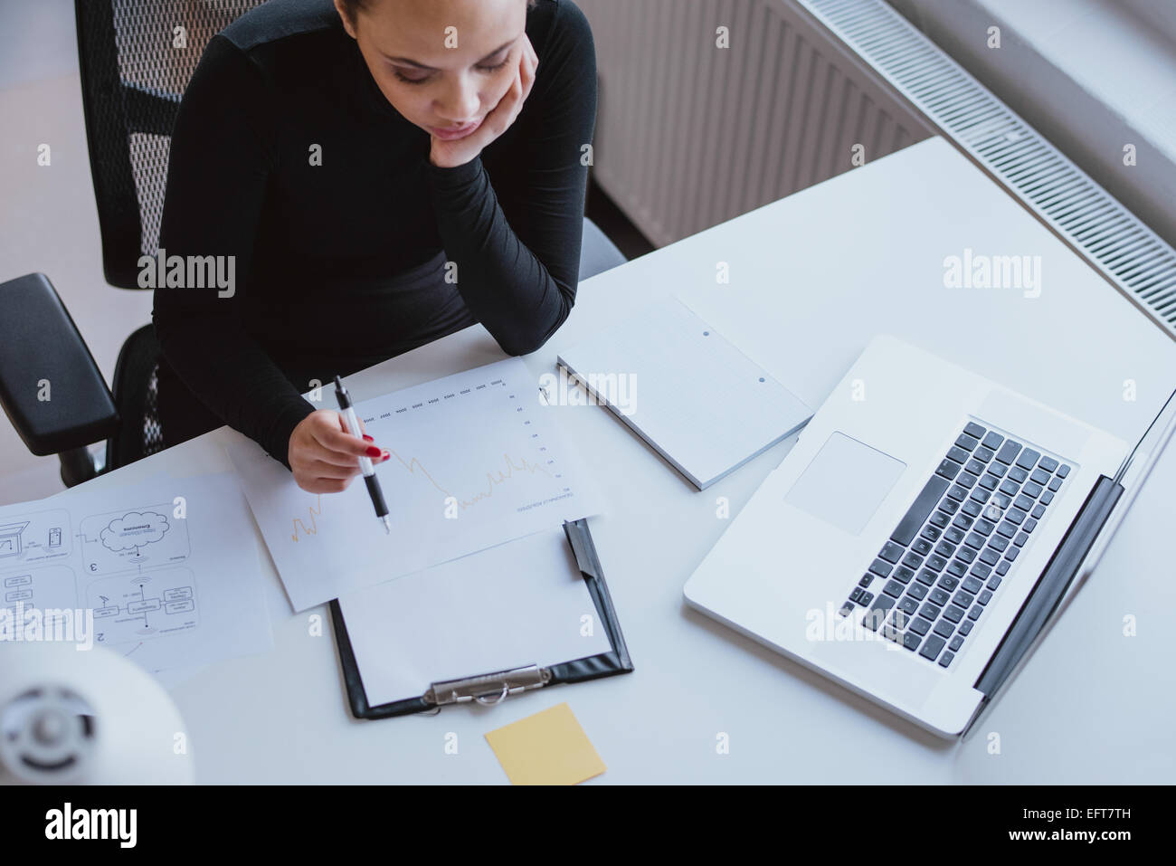 Vista superiore della donna analizzando la crescita aziendale su un grafico mentre è seduto alla sua scrivania in ufficio. Foto Stock