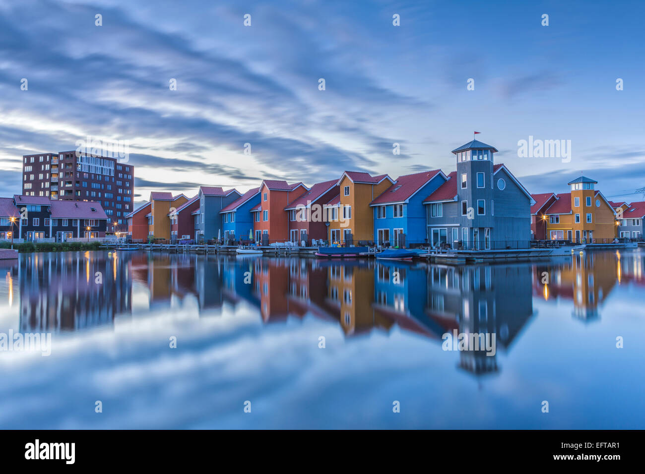 Luminose colorate case di legno riflettendo in acqua con un cielo blu in Olanda al tramonto Foto Stock