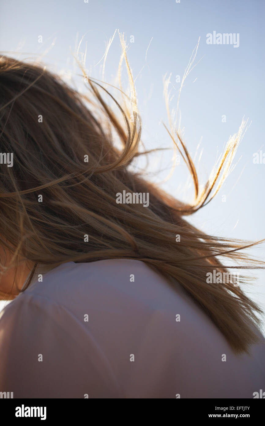 Ritratto di giovane ragazza, lunga retro-illuminato, capelli biondi soffiando nel vento contro il cielo blu Foto Stock
