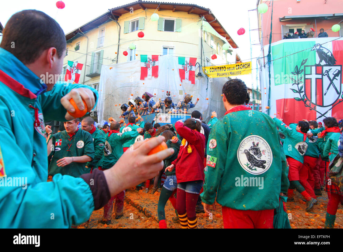 La folla circonda un carrello durante un intenso colore arancione gettando lotta al Carnevale di Ivrea. Foto Stock