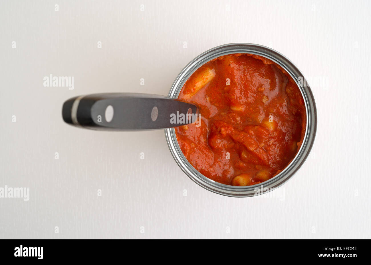 Un aperto può di poco costoso pasta in salsa di pomodoro con un manico nero cucchiaio sulla cima di un tavolo bianco top con finestra naturale luce. Foto Stock
