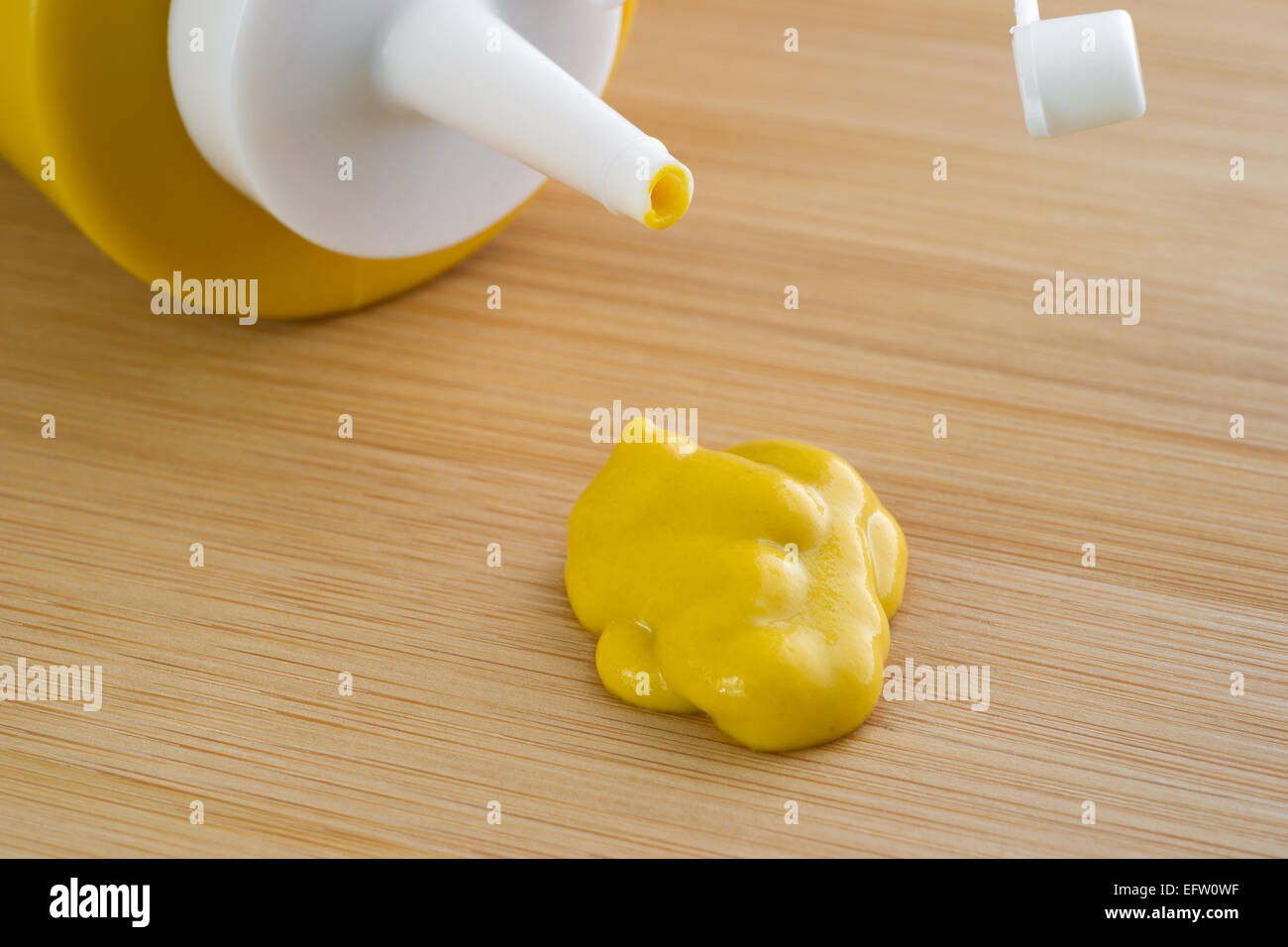 Vista ravvicinata di una bottiglia di senape posa sul suo lato con un piccolo blob spremuto fuori di fronte su di un legno tagliere. Foto Stock