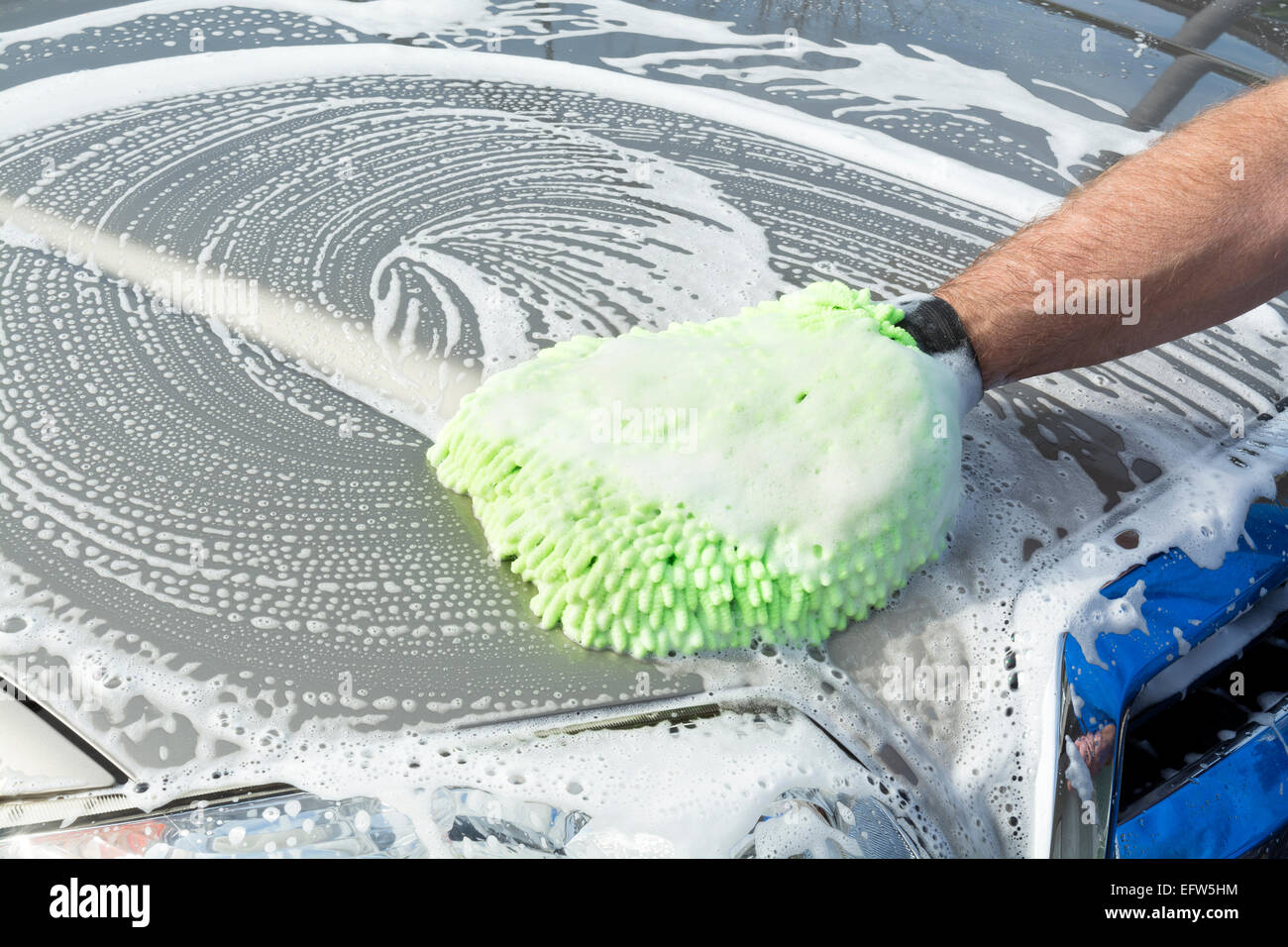 Un uomo utilizza un panno morbido, verde micro guanto in fibra con acqua e sapone per lavare la sua auto. Foto Stock