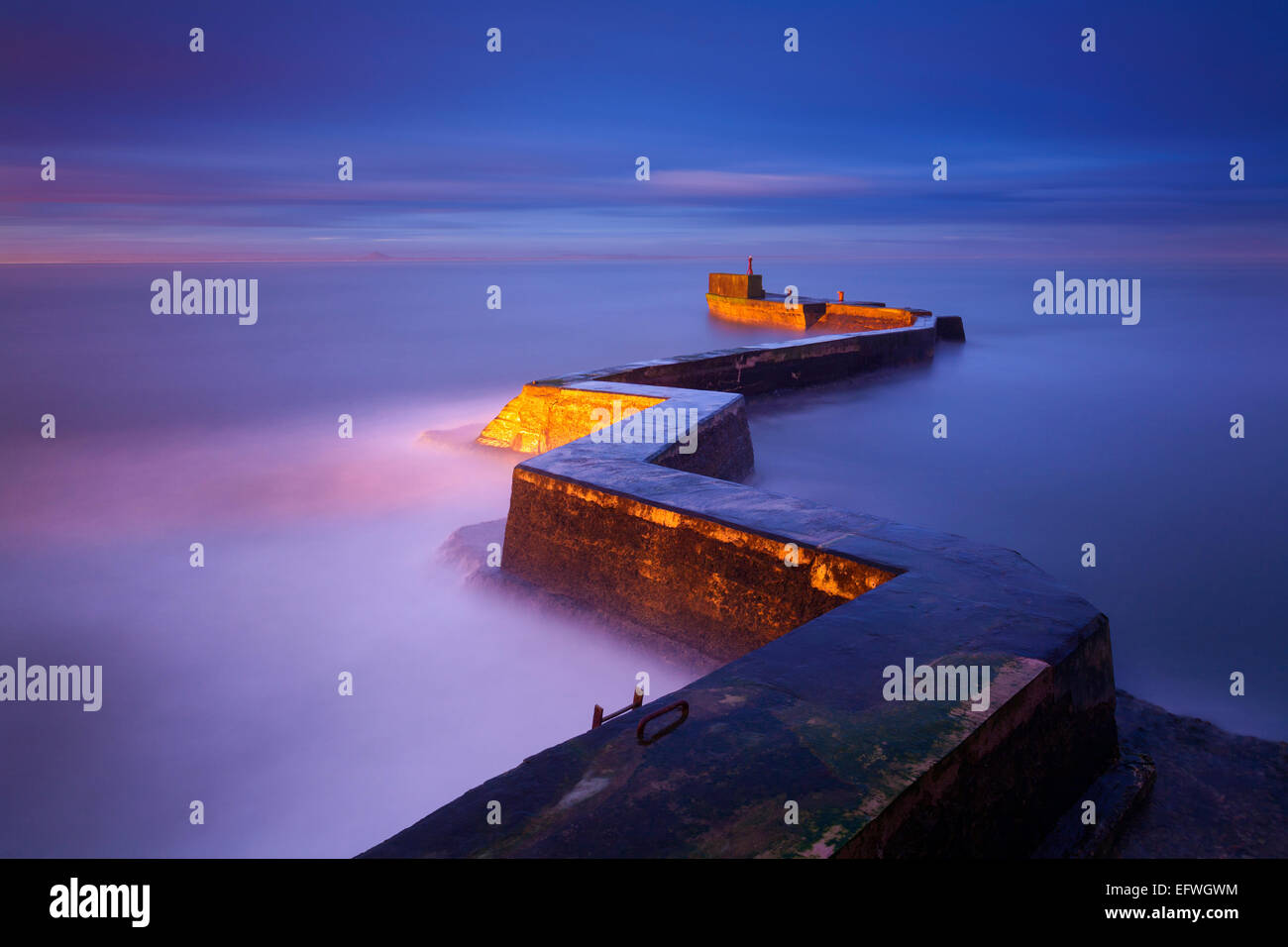 Il sole sorse perpendicolarmente allo zigzag, portando a una luce direzionale meravigliosamente morbida sul frangiflutti dietro il frangiflutti di St Monans Foto Stock