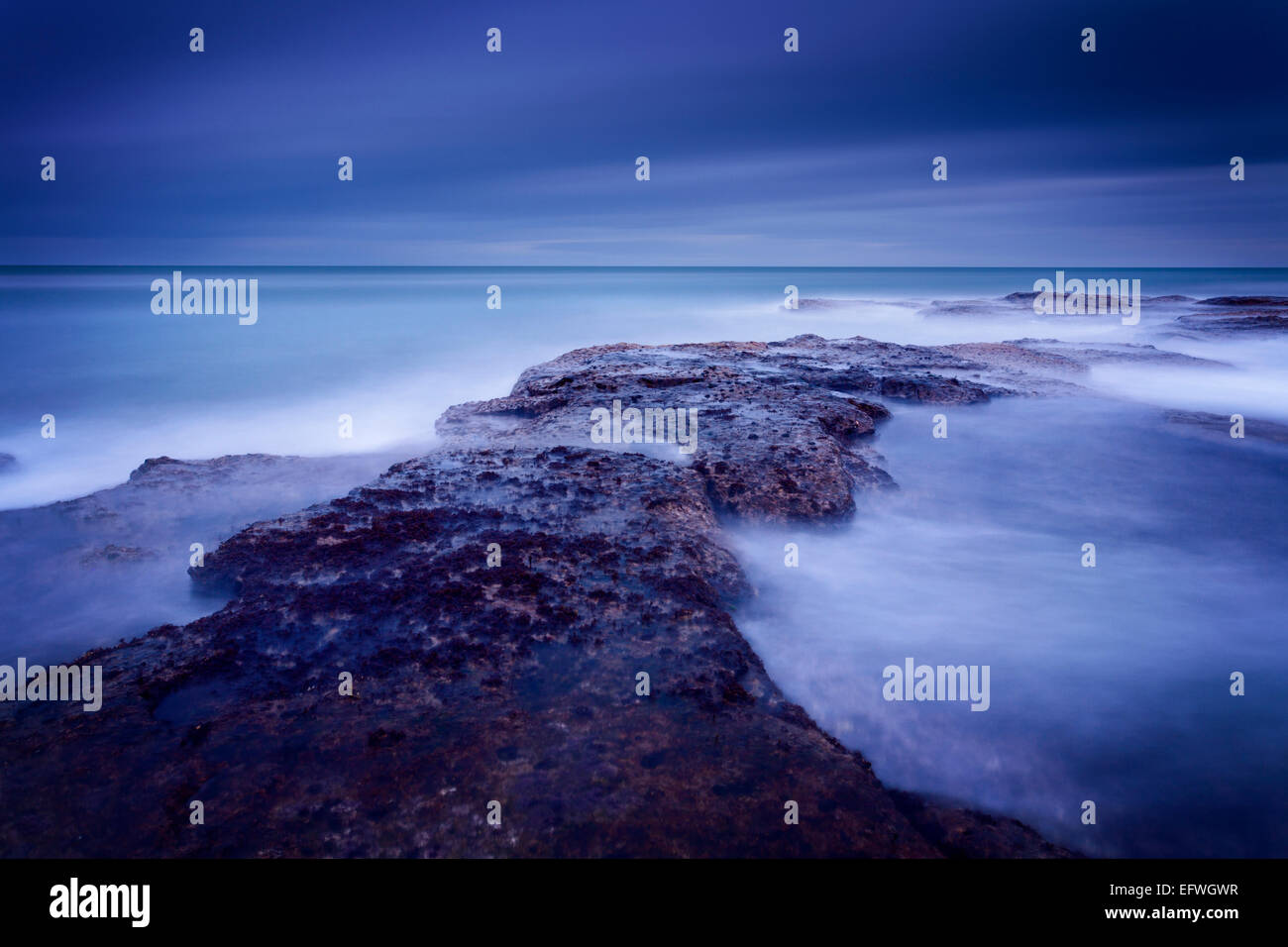 Grandi onde la battitura della barriera corallina di Thorntonloch durante il blu ora prima dell'alba. Foto Stock