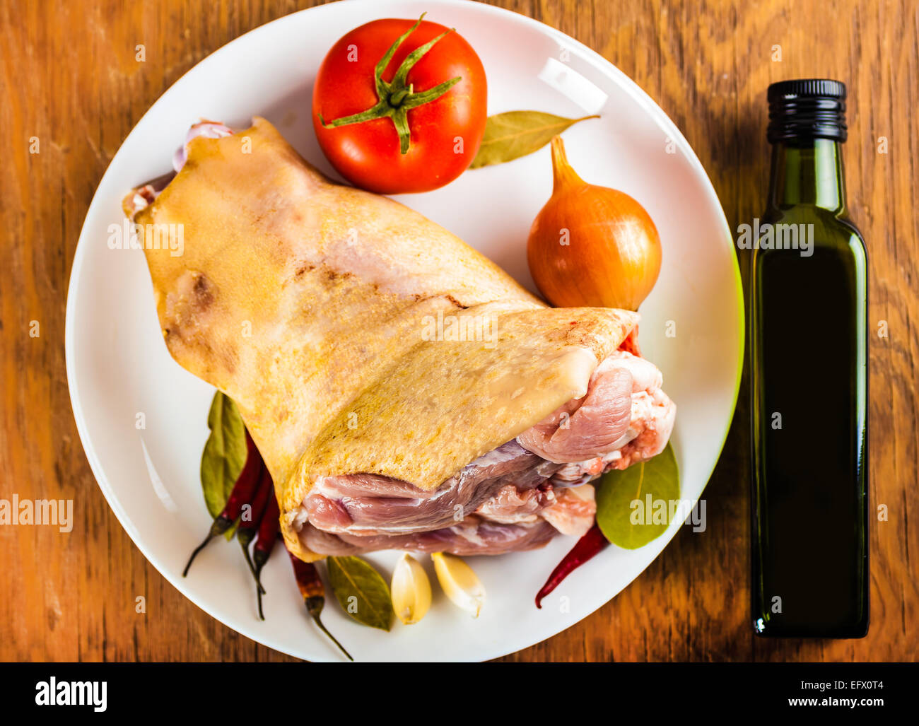 Lo stinco di maiale su di una piastra con spezie e verdure, un sfondo di legno Foto Stock