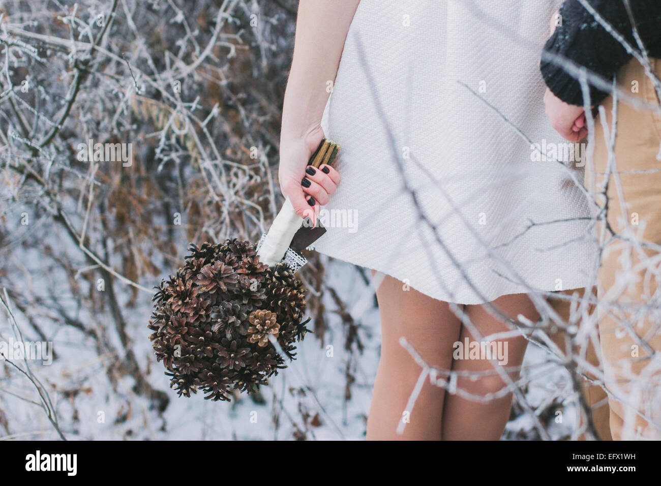 Sposa e lo sposo tenendo le mani nella coperta di neve in inverno foresta; sposa azienda Bouquet nozze fatta di pigne Foto Stock