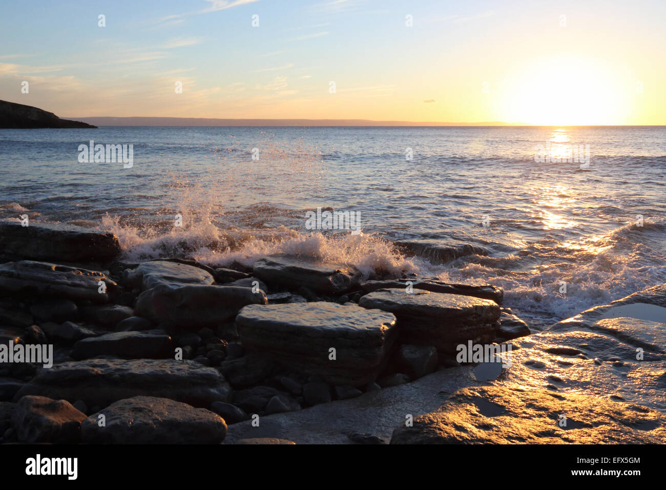 Onde che si infrangono sulle rocce sulla spiaggia di Gallese al crepuscolo Foto Stock