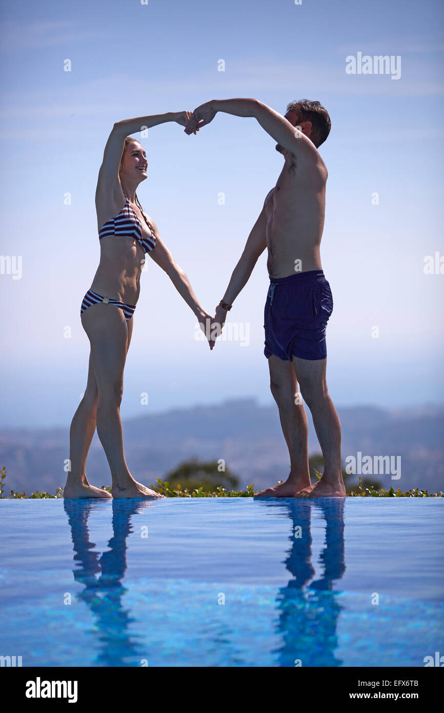 Coppia in vacanza facendo a forma di cuore con i loro corpi in piscina Foto Stock