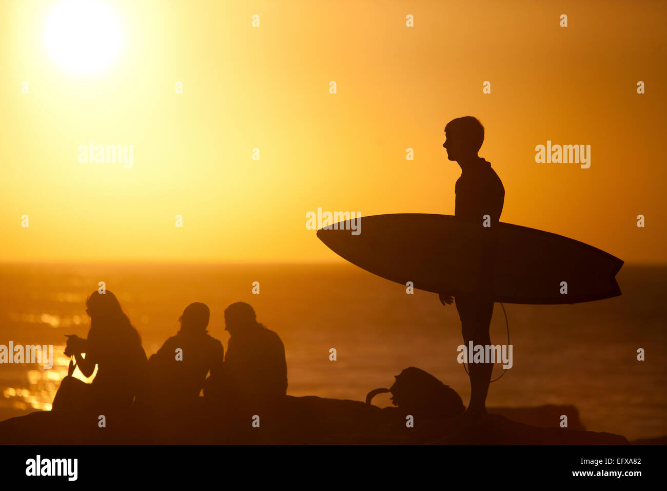Il surfer che trasportano le tavole da surf sulla spiaggia al tramonto, Taghazout, Marocco Foto Stock