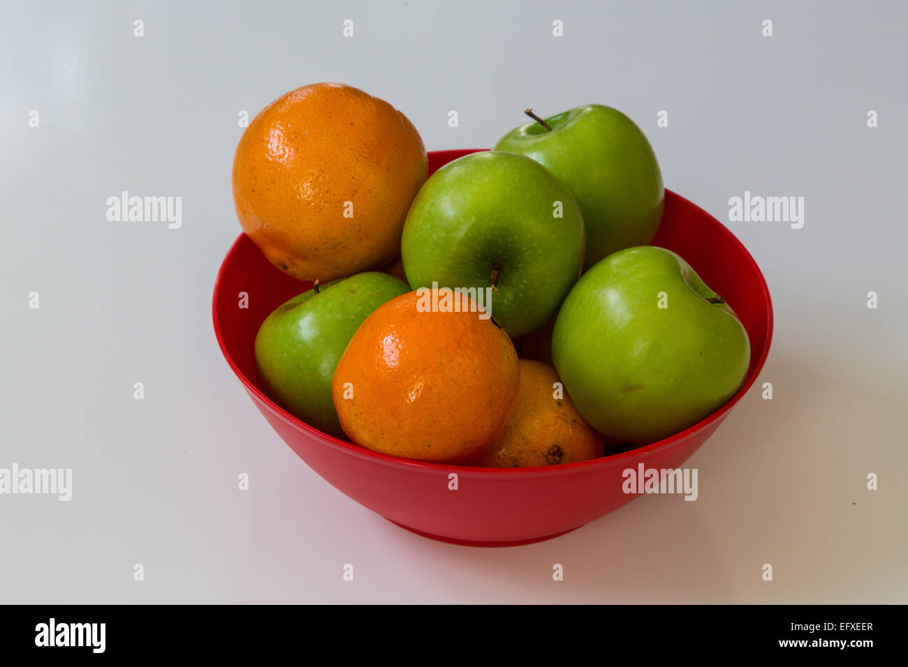 Close-up di fresco verde mele e arance in un recipiente rosso Foto Stock