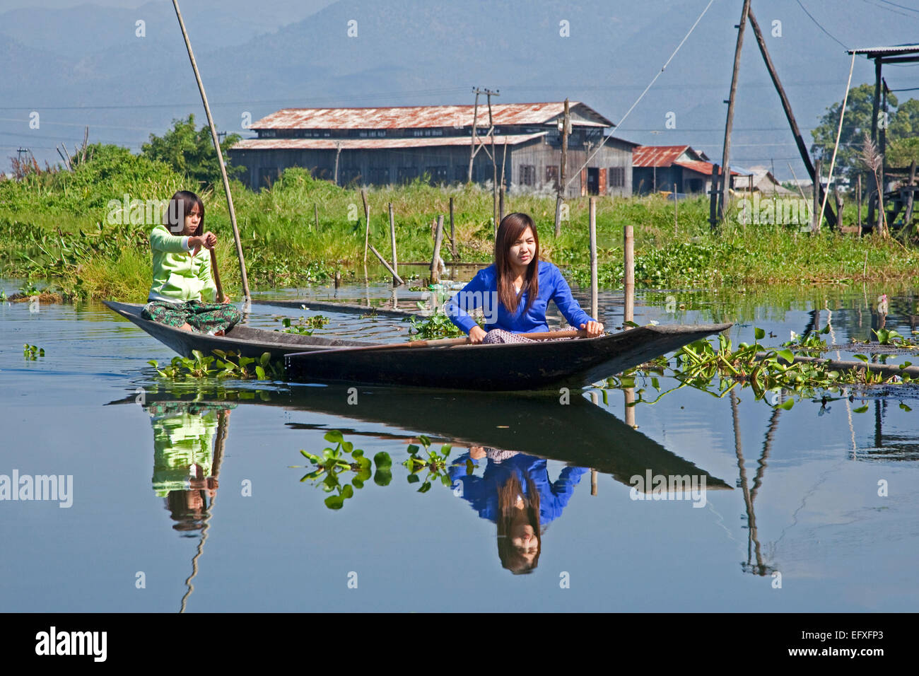 Due donne Intha canottaggio in un tradizionale legno aperto barca / pirogue / proa sul Lago Inle, Nyaungshwe, Stato Shan, Myanmar / Birmania Foto Stock