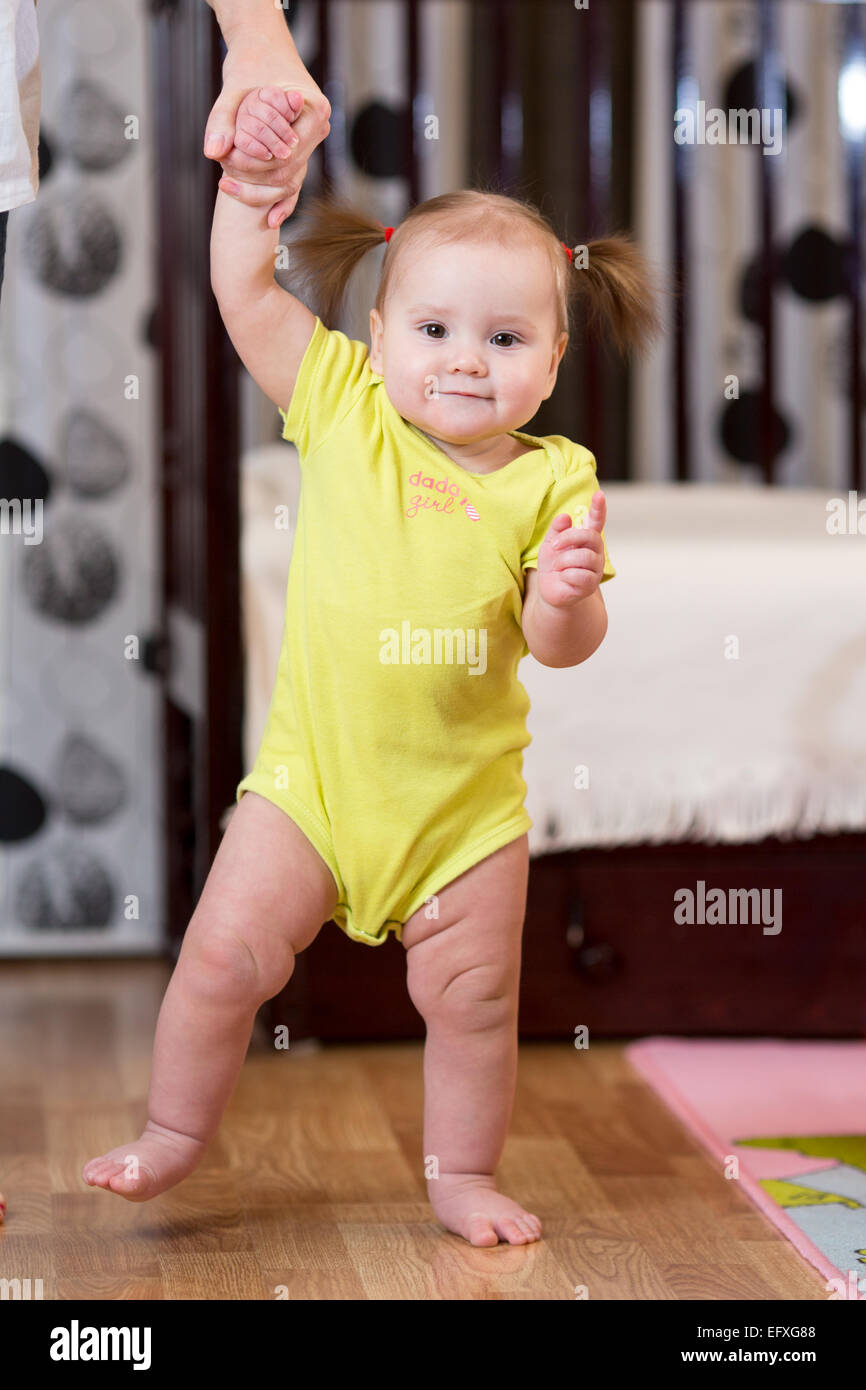 Baby prendendo i primi passi con la madre aiutare Foto Stock