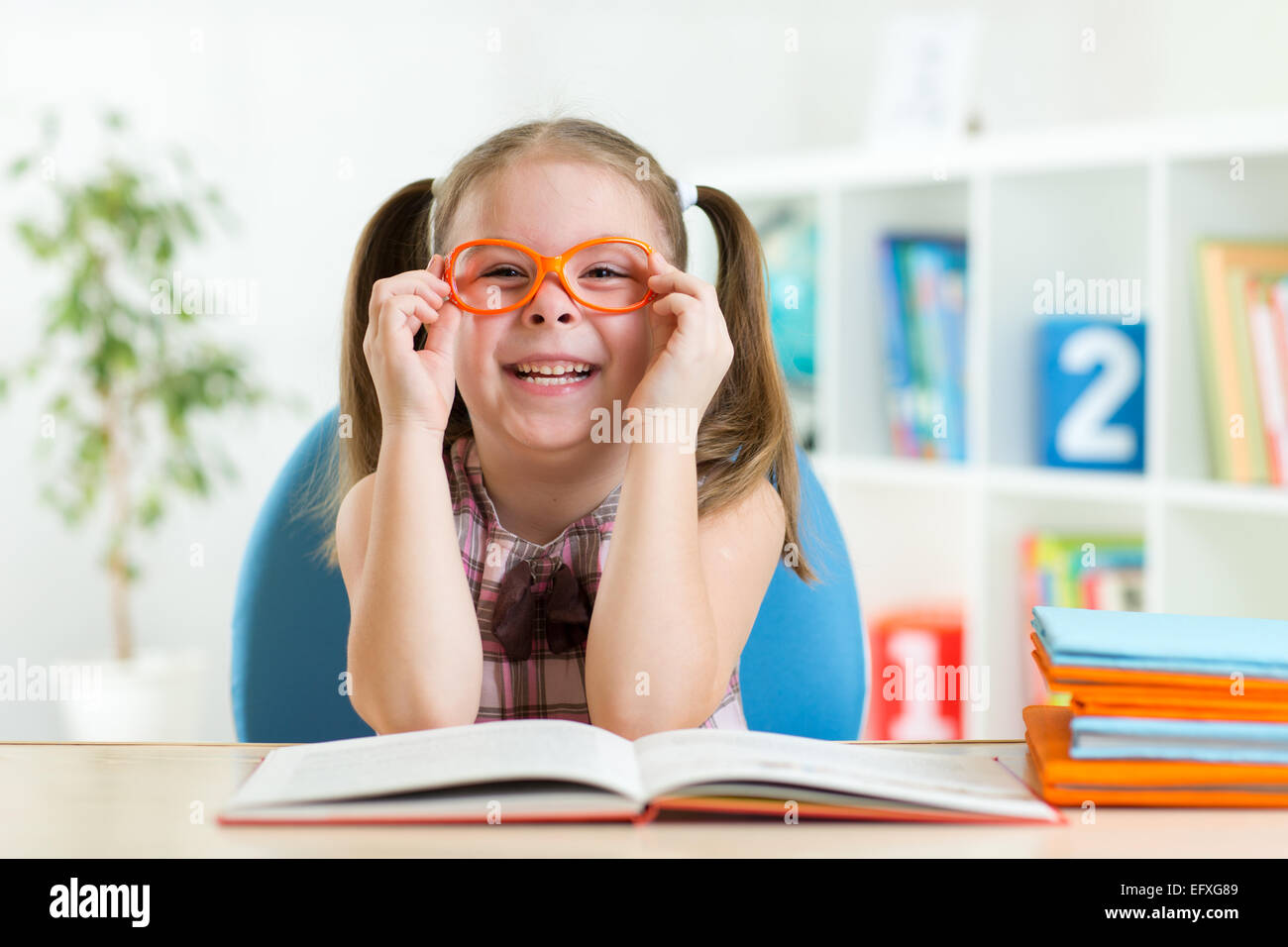 Carino bambina la lettura di un libro mentre con gli occhiali Foto Stock