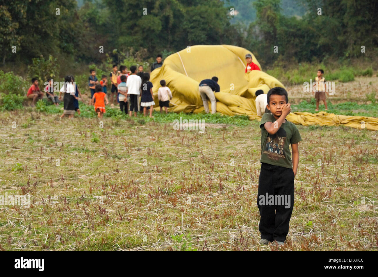 Vista orizzontale di giovani laotiani bambini aiutando a riporre una mongolfiera sbarcati vicino al loro villaggio. Foto Stock