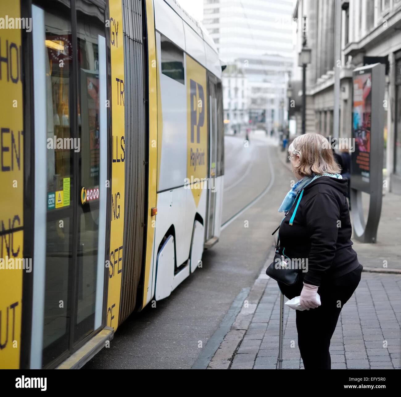 Una donna in attesa di attraversare la strada mentre un Nottingham express transit il tram passa da. Inghilterra, Regno Unito Foto Stock