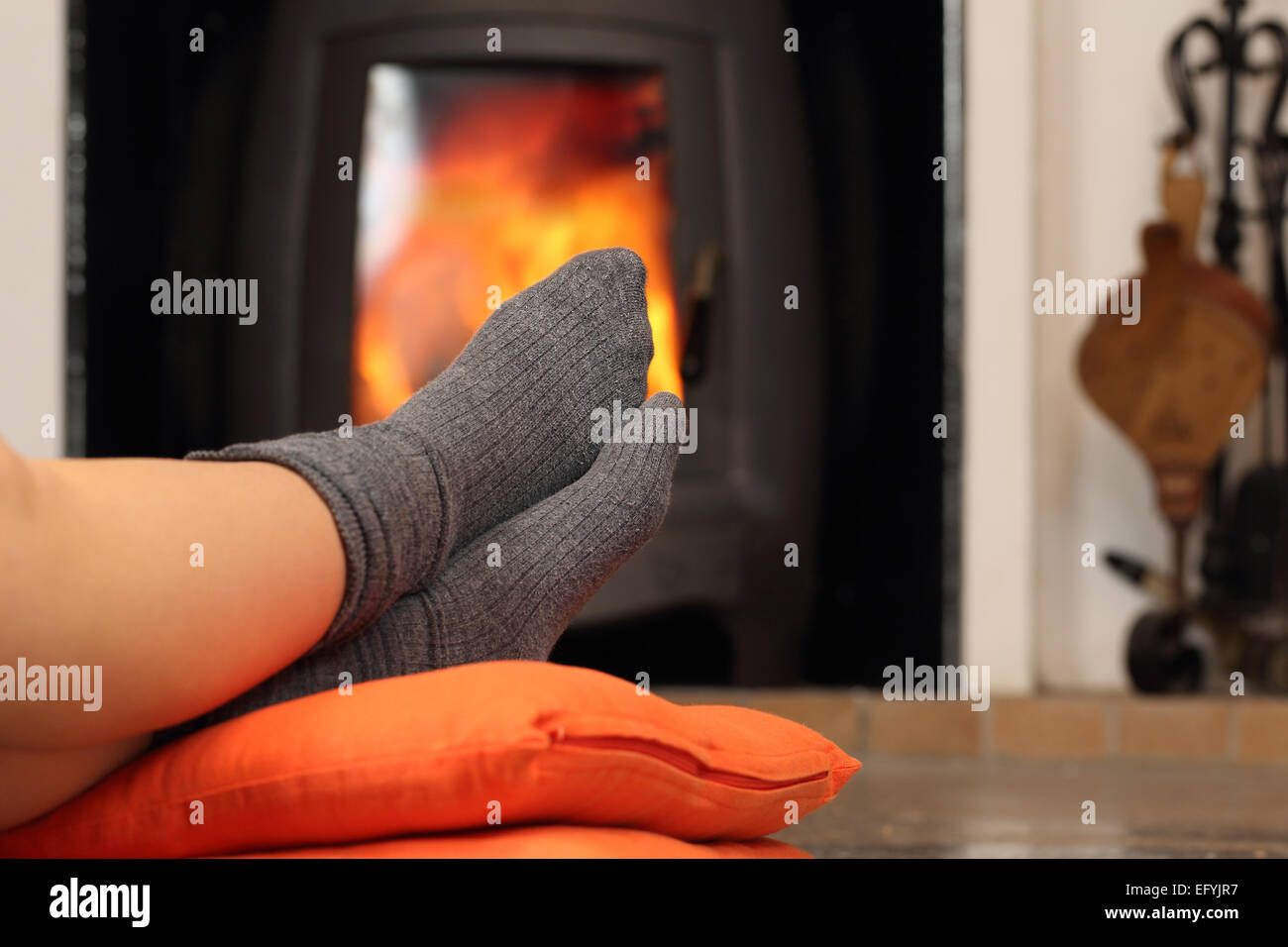 Piedi di donna con calze in appoggio vicino al caminetto con un background di calore Foto Stock