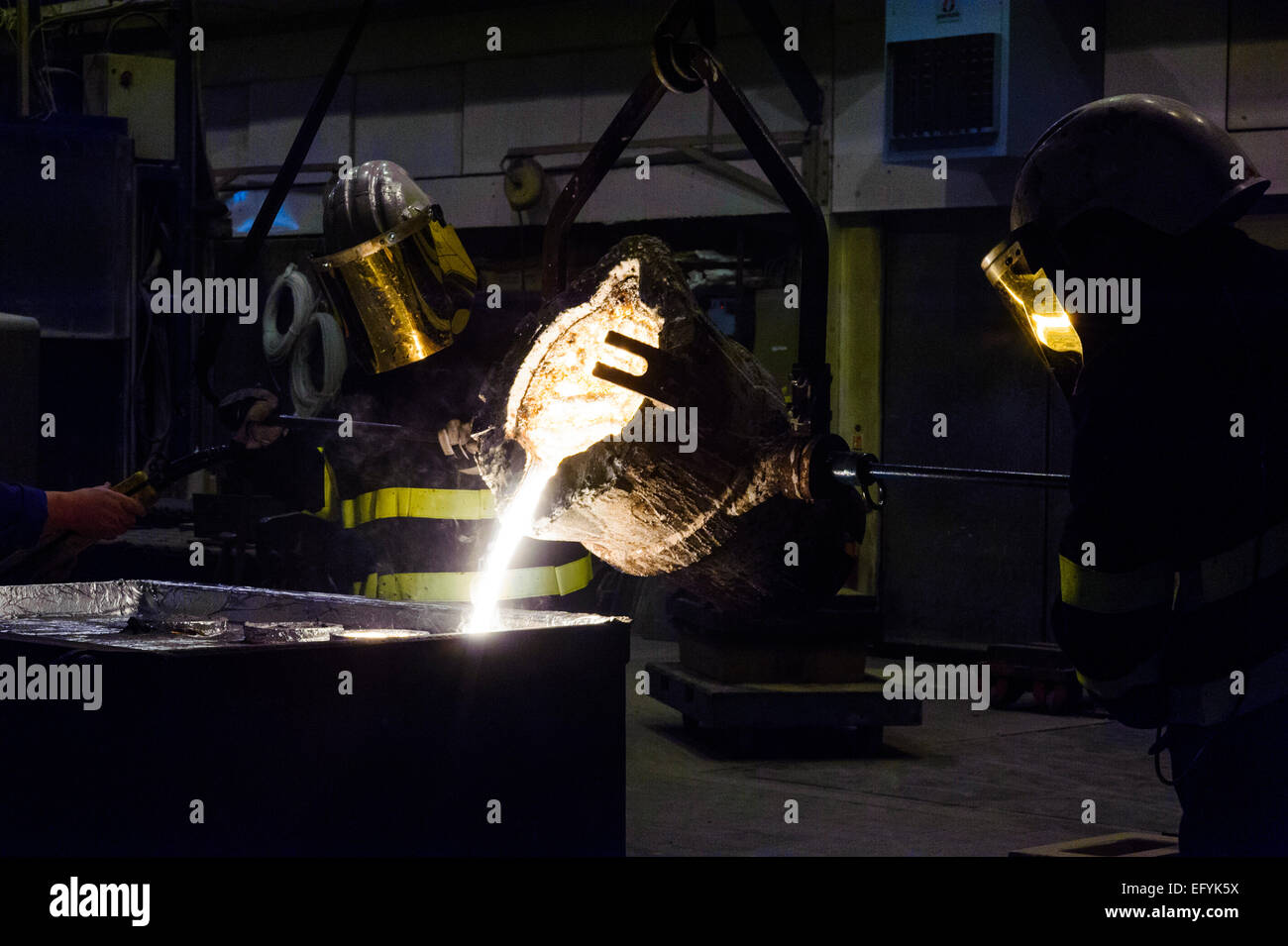 Lavoratori fonderia di versare il metallo fuso da un forno utilizzando un crogiolo in calchi di sabbia Foto Stock