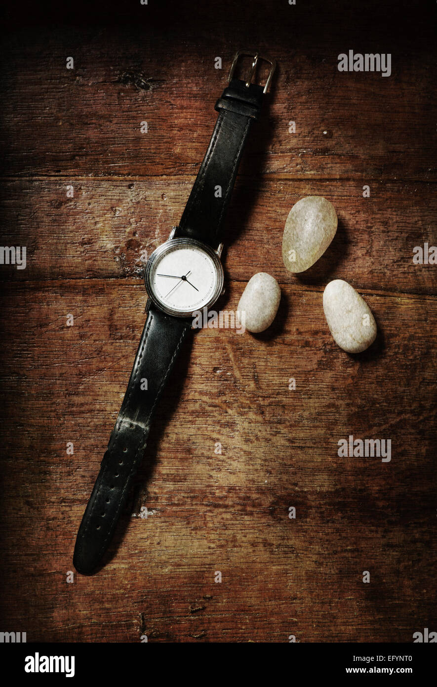 Vita Tranquilla con l'orologio al polso e tre pietre sul tavolo di legno. Vista dall'alto. Foto Stock