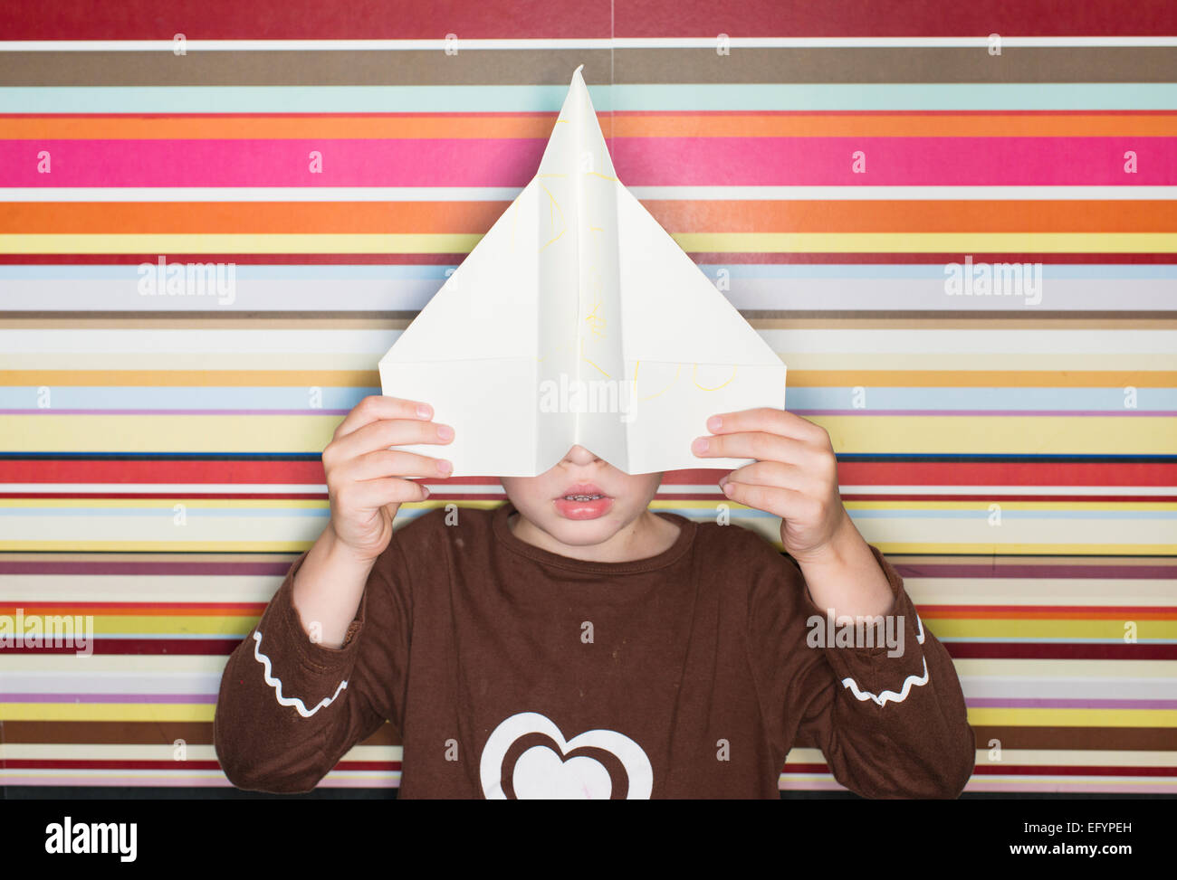 Bambino azienda aeroplano di carta nella parte anteriore del viso Foto Stock