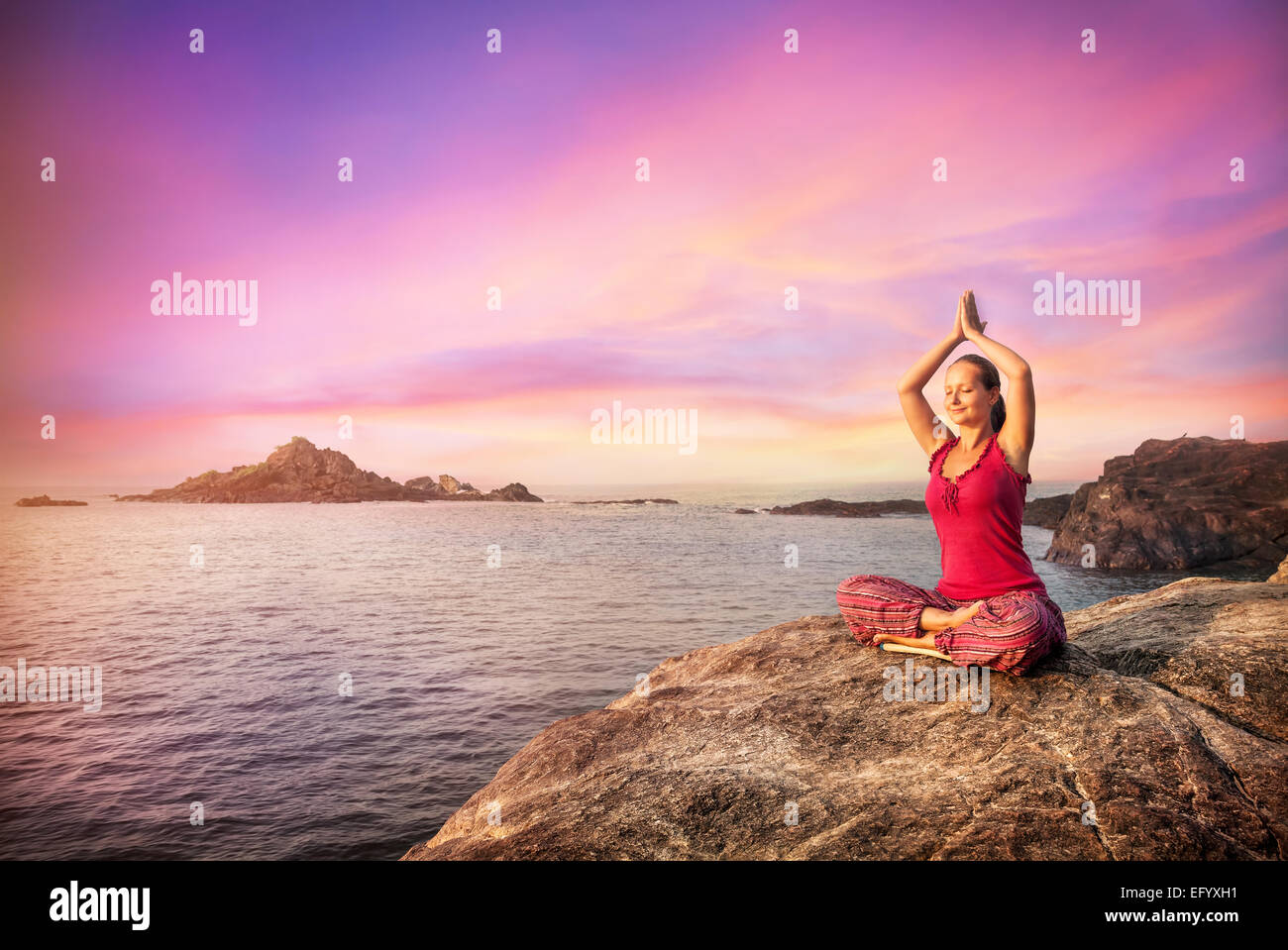 Donna di fare meditazione in costume rosso sulla pietra vicino all'oceano in Gokarna, Karnataka, India Foto Stock