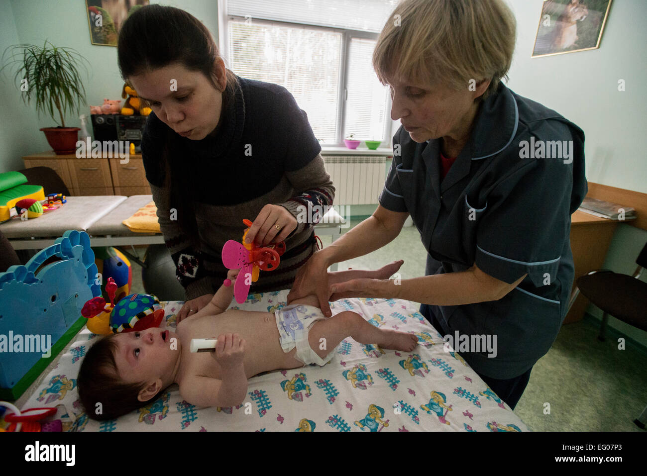 Madre, rifugio dalla città Gorlivka nella regione di ATO, calma giù il suo bambino disabili mentre ricevendo la terapia di massaggio, orfanotrofio "Zhytomyr regionali di casa dei bambini", Ucraina. 2 febbraio 2015. "Zhytomyr regionali di casa dei bambini' ha 67 bambini orfani da neonati a 4 anni di età. 25% di loro hanno mentale, disabilità intellettuale, HIV. Orfanotrofio ha più di 90% di adozione. Sin dal 2008 anno Ucraina fornendo programma di smantellamento orfanotrofio governativa, incluso il "Zhytomyr regionali di casa dei bambini". Foto di Oleksandr Rupeta Foto Stock