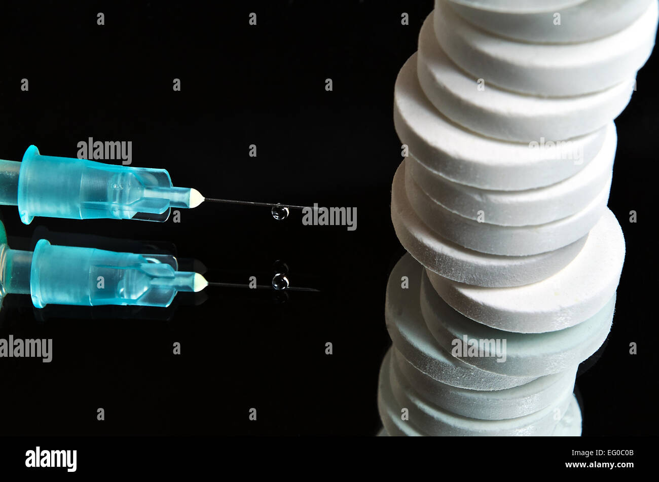 Pills impilati uno sull'altro con un ago medicale avente una goccia di liquido appeso. La superficie a specchio Foto Stock