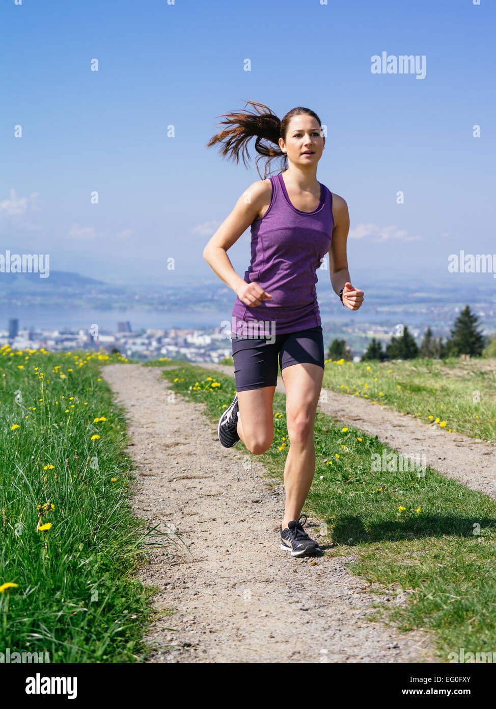Foto di una giovane donna jogging ed esercitando su di un percorso di paese. Il lago e la città di distanza. Una leggera sfocatura visibile. Foto Stock