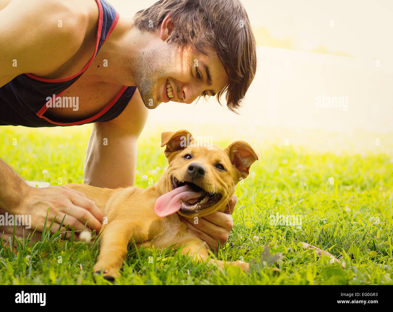 Uomo sorridente sdraiati sull'erba accarezzare il suo cucciolo di cane Foto Stock