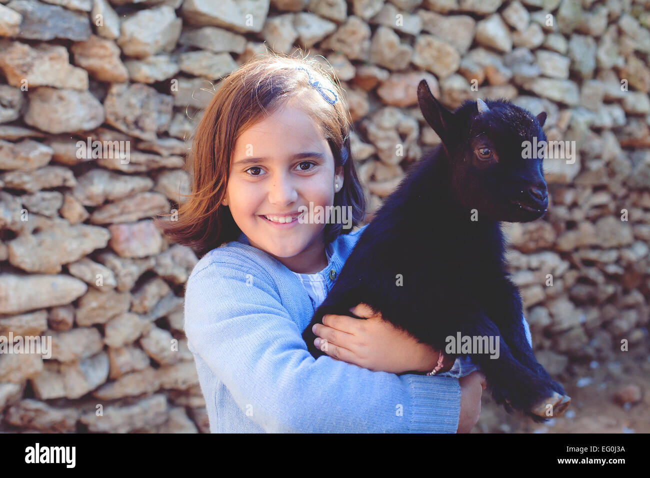 Sorridente ragazza in piedi da una parete che porta una capra bambino Foto Stock