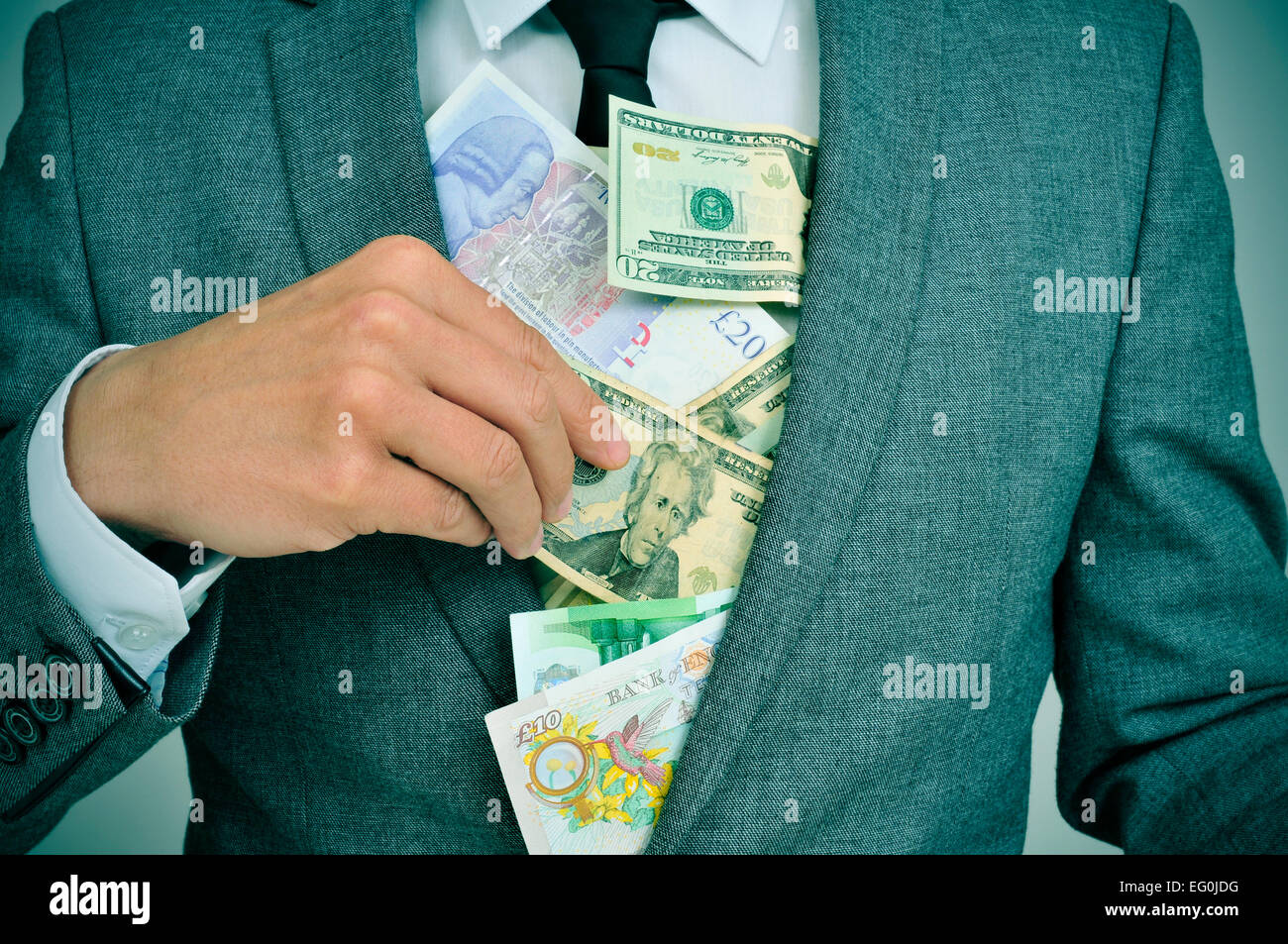 Uomo in tuta mettendo euro, dollaro e sterlina inglese e le fatture nella sua giacca, raffiguranti i concetti come la golosità, corruzione o misappropri Foto Stock